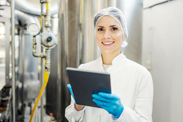 A female milk factory supervisor using tablet and smiling at the camera.