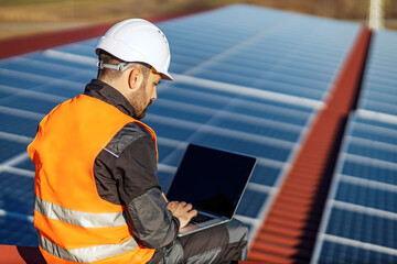 A worker testing solar panels on the laptop on roof.