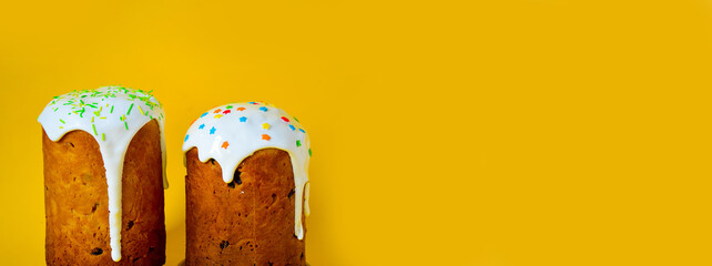 High traditional Easter cakes with white meringue and icing, colored sprinkles on a yellow background on the left. Banner. Free space for the inscription. Easter concept. Baking with your own hands.