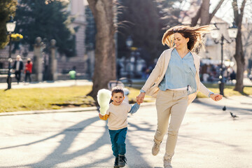 A happy son and mother holding hands and running in park.