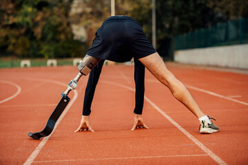 Rear view of handicapped runner in start position for run at stadium on running track.