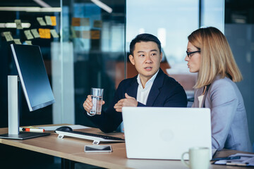 Two employees are having fun. Asian man and blonde woman taking a break, colleagues working together in a modern office