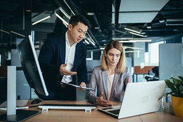 Two employees in a modern office, an Asian man and a woman working at a table, colleagues...