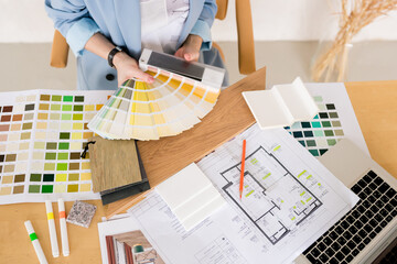 Woman architect working on interior renovation in workplace. Designer choosing color samples according to the visualization and blueprints of the project. Architecture and interior design concept.