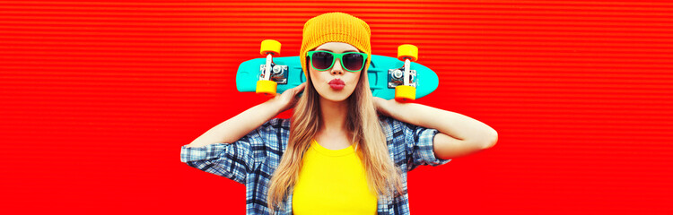 Portrait of stylish blonde young woman model with skateboard wearing colorful yellow hat on red background