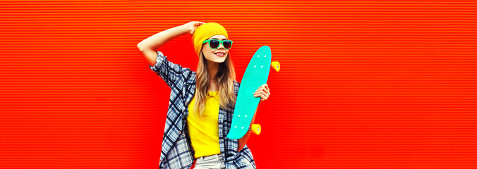 Portrait of stylish young woman model with skateboard wearing colorful yellow hat on red background