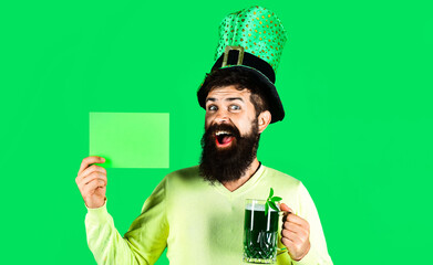 Patricks Day. Happy Bearded man in hat with green beer holds board with copy space for advertising.