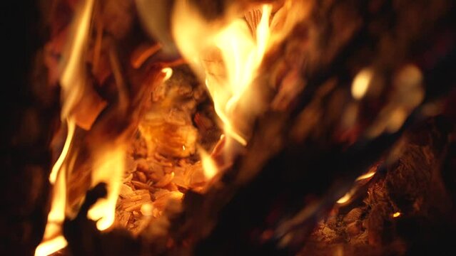 This close up video shows a macro view of wood burning and bright flames and ashes against a contrasting black night background. 