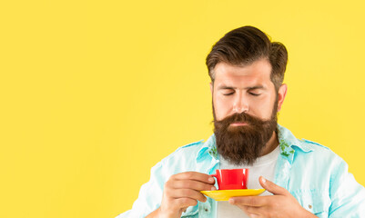 Portrait of man smelling tea holding cup and saucer yellow background, copy space