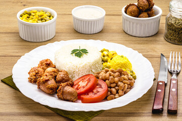 plate with typical Brazilian meal, sausage and fried chicken, rice with beans and salad, farofa and fried egg