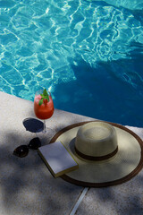 Fototapeta na wymiar watermelon cocktail with straw, sunglasses and book hat on pool
