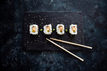 Japanese sushi food rolls served on blackboard plate, dark background - top view