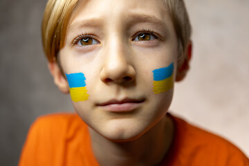 a child against war, a thoughtful boy with a painted flag of Ukraine on his cheeks looks up and dreams of world peace