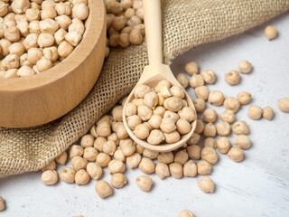 Wooden bowl and wooden spoon full of chickpeas on a light concrete background. close-up