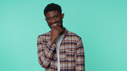 Cheerful lovely african american bearded adult man in casual checkered shirt smiling and looking at camera. Young guy with brown eyes indoor studio shot isolated on blue background. Male nature beauty