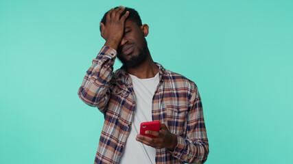 African american adult man in shirt use mobile cell phone typing browsing, loses becoming surprised sudden lottery results, bad fortune, loss. Young guy on blue background. People sincere emotions