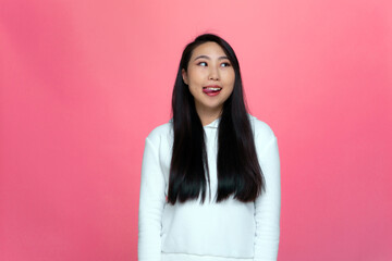 Fototapeta premium Playful asian young modern girl fooling around showing tongue, looking aside with lively on pink studio background