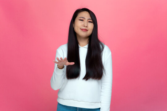 Modern asian girl student shows so-so gesture with skepticism on pink studio background. Doubts, uncertainty