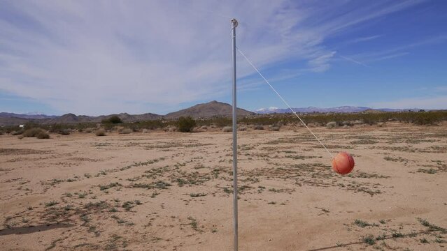 This wide shot, surreal video shows an old, remote tether ball wrapping around a pole in the desert.