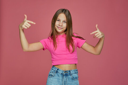 Cool confident child girl pointing to herself, proud of own success, gesturing like a rapper on pink studio background