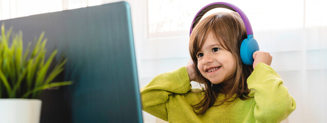 Horizontal banner or header with elementary schooler girl in headphones sitting at desk on laptop -...