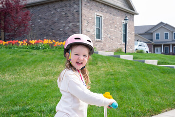 Cute little girl riding a scooter on a sidewalk in residential neighborhood