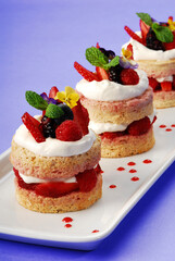cake or sponge cake with red berries and edible flowers layered with whipped cream on lilac background, summer cake