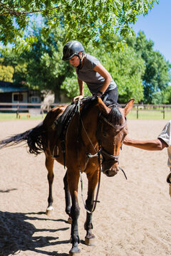 latina female apprentice rider riding a horse in a stable, vertical photo