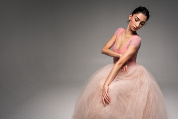 Fototapeta premium young pretty, fragile, beautiful ballerina dancing in a long pale pink dress with a tulle on a uniform background, hand movements, restrained tone. Ballet, dance, dancer. Place for inscription