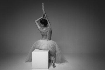 black and white photo, young pretty, fragile, beautiful ballerina sitting on a white square,...