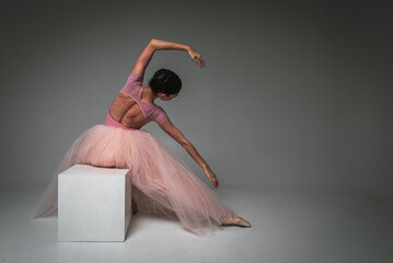 young pretty, fragile, beautiful ballerina sitting on a white square, inverted raised hands in a...