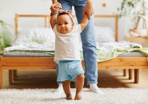 Happy Ethnic Baby Girl Takes Her First Steps Smiling And Holding Her Mother's Hands