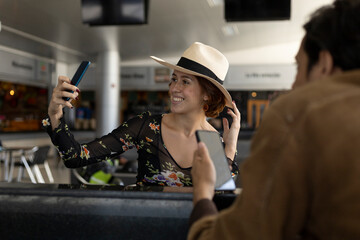 Young Latin American girl (22) with cowboy hat is on vacation and takes a self-portrait with her cell phone. Concept of technology.