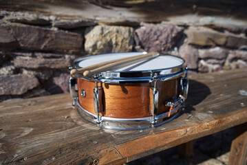 Drum with drumsticks on a wooden ground in front of a stone wall