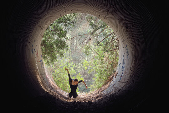 Flexible woman dancing ballet in tunnel in forest