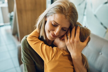 Loving mother embraces her sad little girl and consoling her at home.