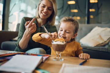 Little girl has fun with whipped cream while eating dessert with her mother.