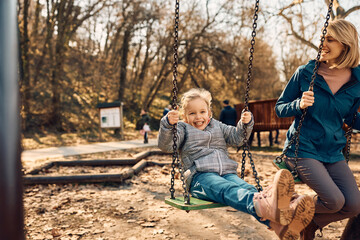 Cheerful little girl swinging with her mother in the park.