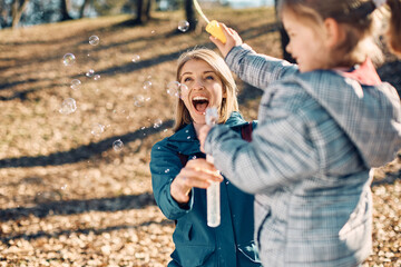 Cheerful mother and daughter have fun with bubble wand in nature.