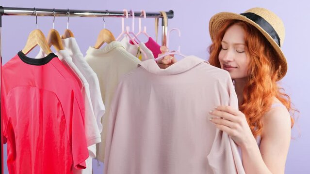 Young redhead woman consumer in a hat being in the shop chose the clothing she liked and smeling it while hugs.