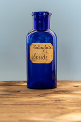 ancient apothecary blue jar with a label where it is written "salicylate de Soude" in french for medicine. the pot is isolated over grey background on wooden table. translation : sodium salicylate