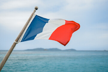 The French tricolor flag flies on the back of the yacht, against the backdrop of the coastal...