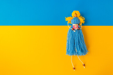 Symbol of Ukrainian nation is a handmade doll knitted from yellow and blue threads. On the paper flag of Ukraine.
