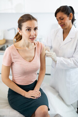 Portrait of smiling young adult woman getting injection during visit at doctors office