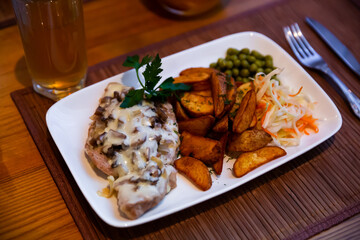 Oven baked pork steak with mushrooms and cheese served with grilled potato and vegetables