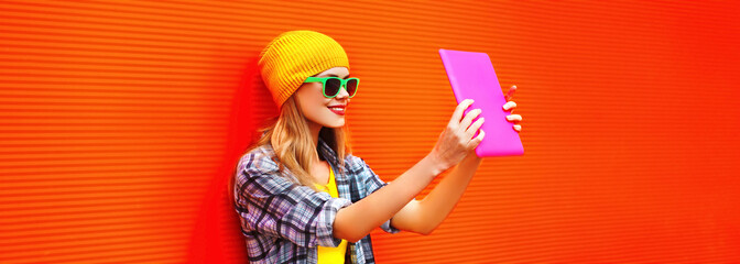 Portrait of stylish cool young woman using tablet pc with skateboard wearing colorful clothes on...