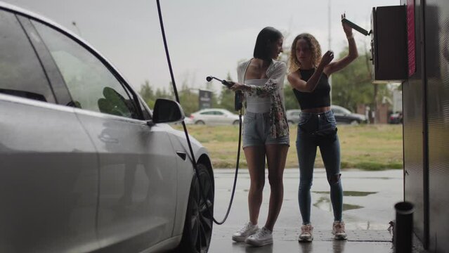 Beautiful girls washing car with high pressure water jet at car wash..