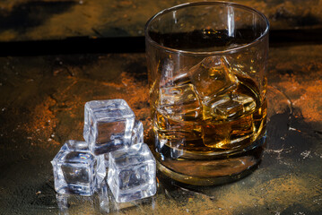 glass of whiskey with ice cubes on a glass brown table.