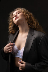 Portrait of a young red-haired curly sexy girl in a jacket with long hair in the studio. Dramatic photo in dark colors.