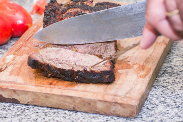 Cook cutting roasted Argentine chorizo steak with a sharp knife on a wooden cutting board. Grass-fed meat.